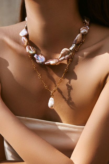 Baroque pearl pendant necklace in layered design showcasing unique pearls and 18k gold chain on a model.