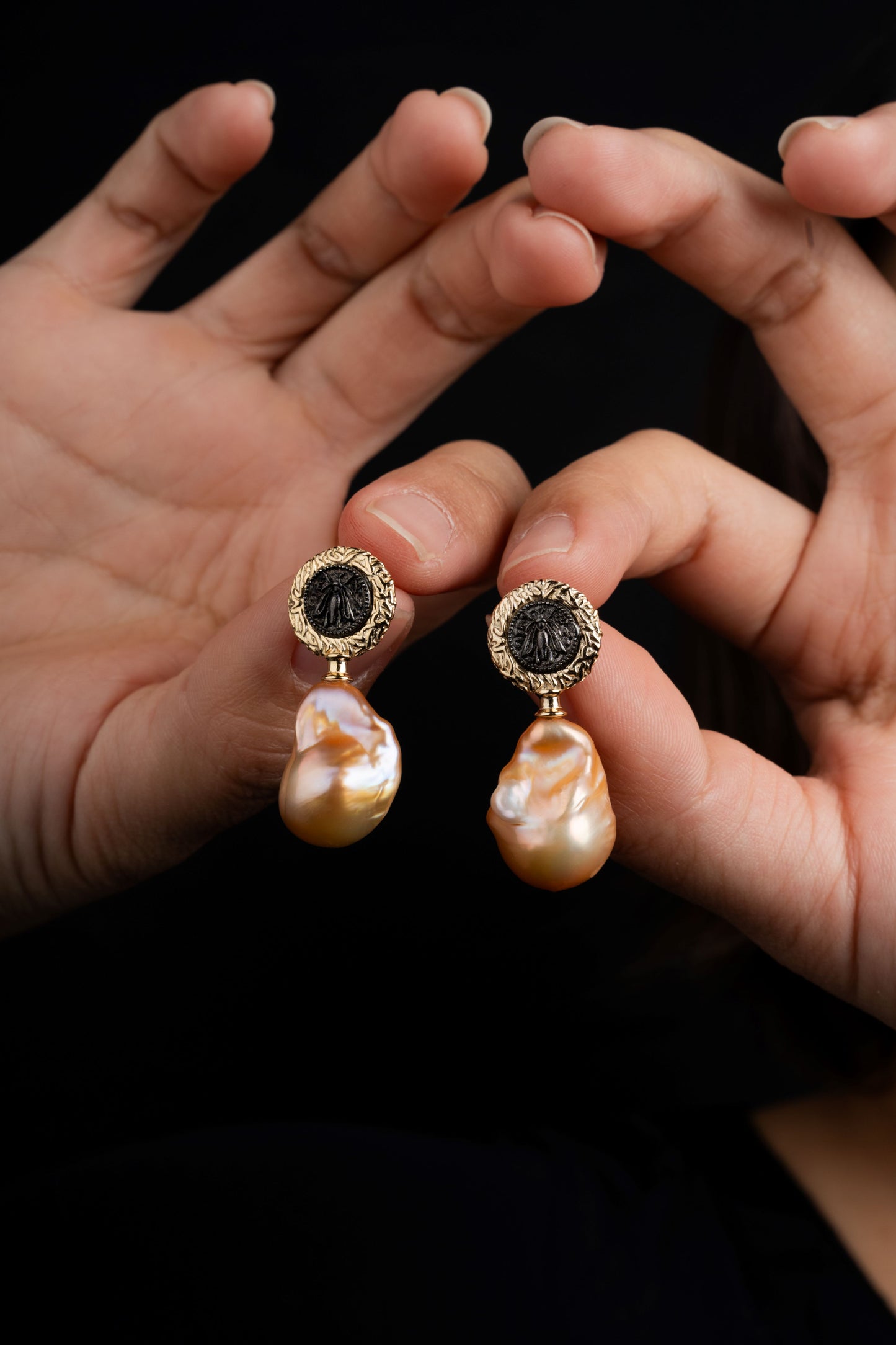 Pearl earrings held between two hands against a dark background