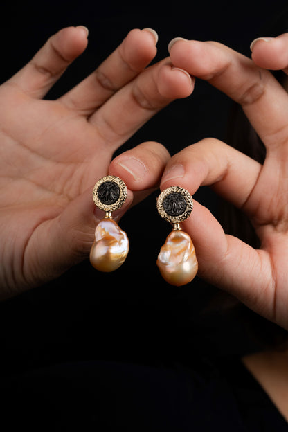 Pearl earrings held between two hands against a dark background
