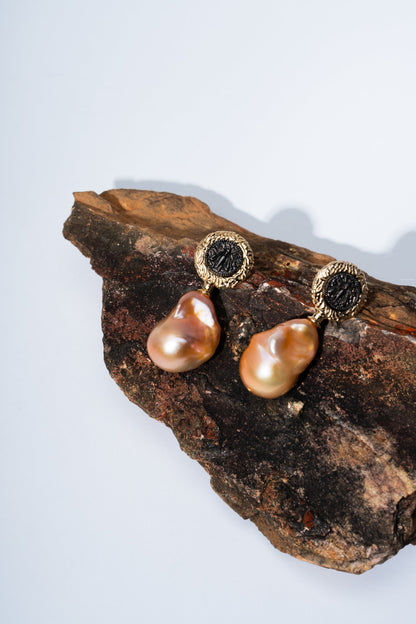 Pair of gold earrings with brown pearls on a wooden surface