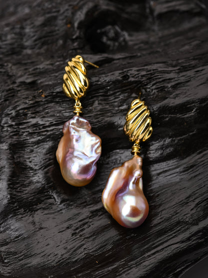 Pair of pearl earrings with gold hooks on a dark textured surface