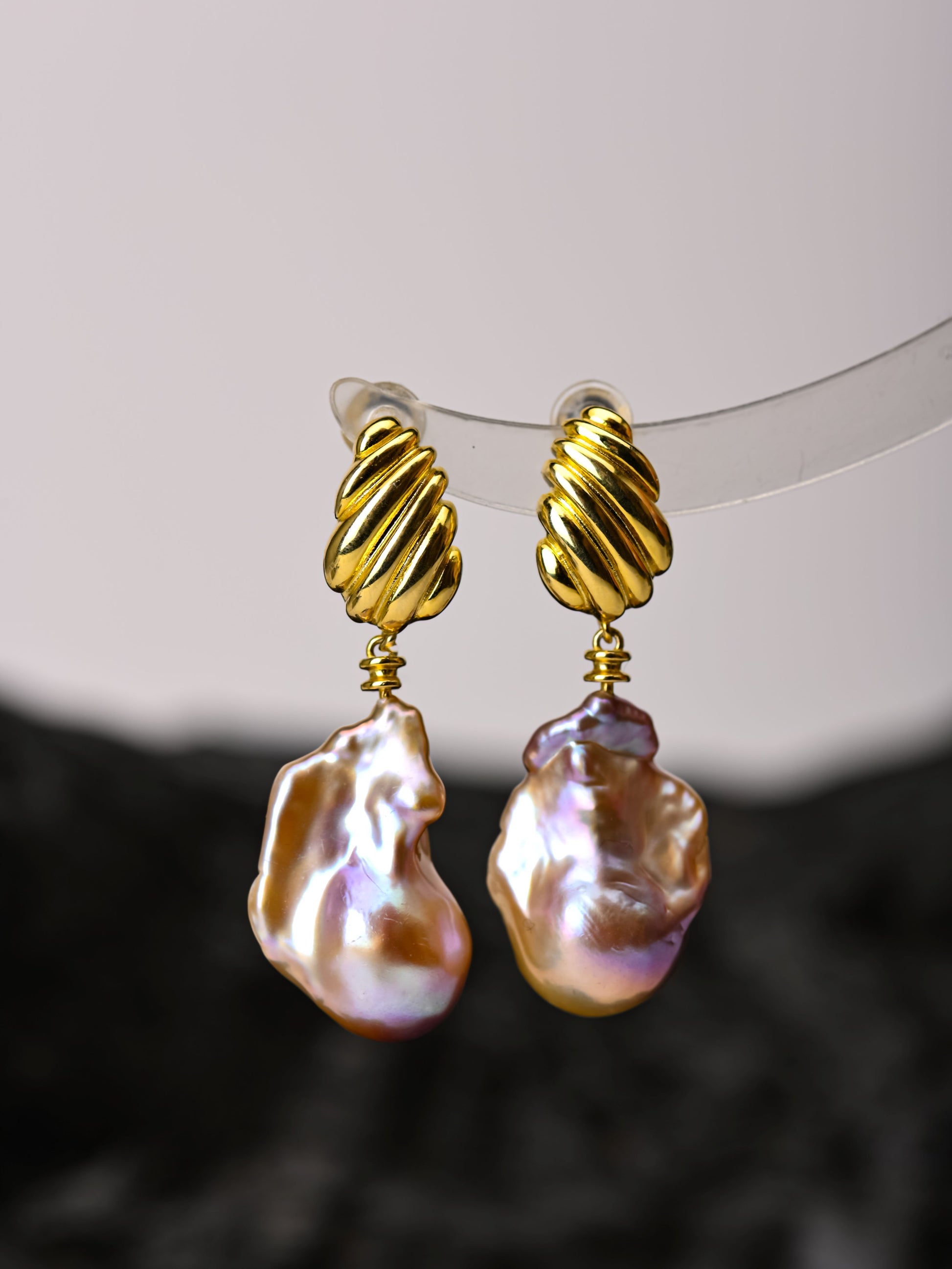 Gold-rimmed baroque pearl earrings on a white background