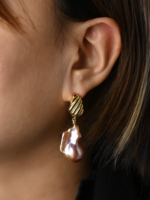 Gold earring with a large pearl drop worn by a person.