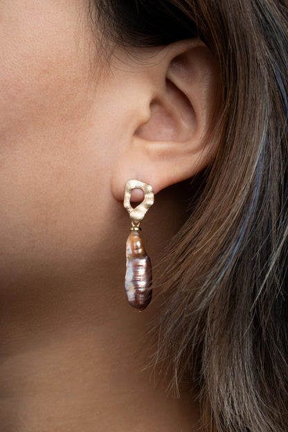 Close-up of a baroque pearl gold earring worn by a person with a neutral background