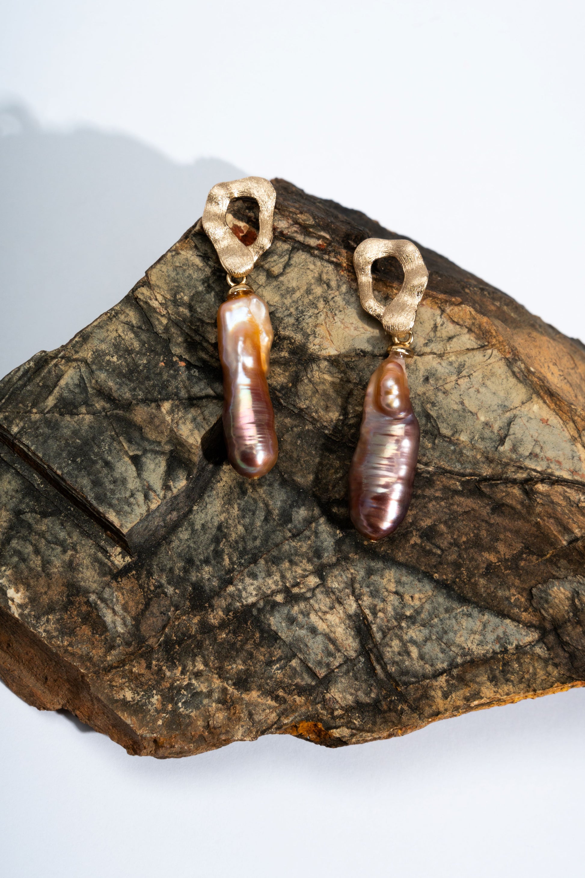 Pair of baroque pearl earrings with brown beads on a textured stone surface