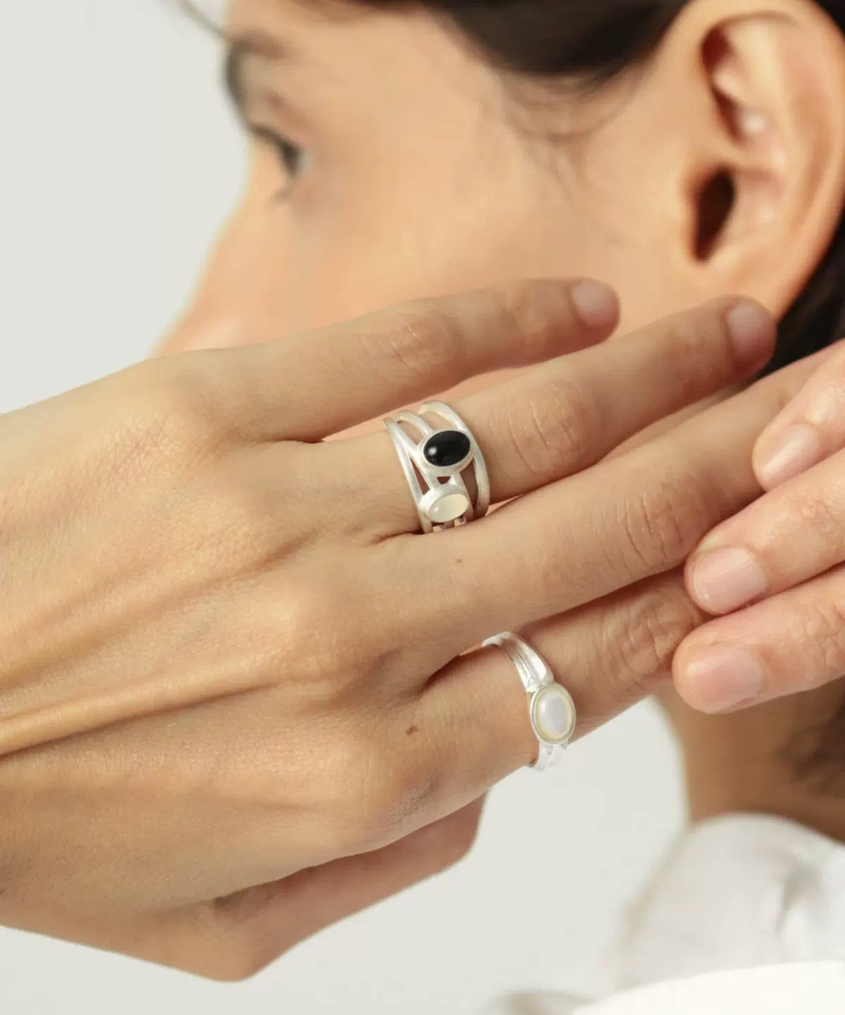 Close-up of a person wearing two silver rings with black and white stones on a neutral background