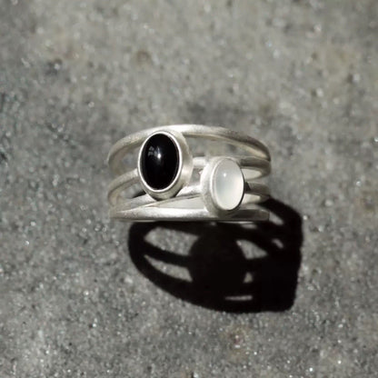 Silver ring with black and white gemstones on a gray surface