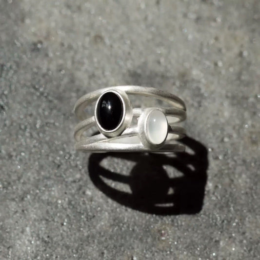 Silver ring with black and white gemstones on a gray surface