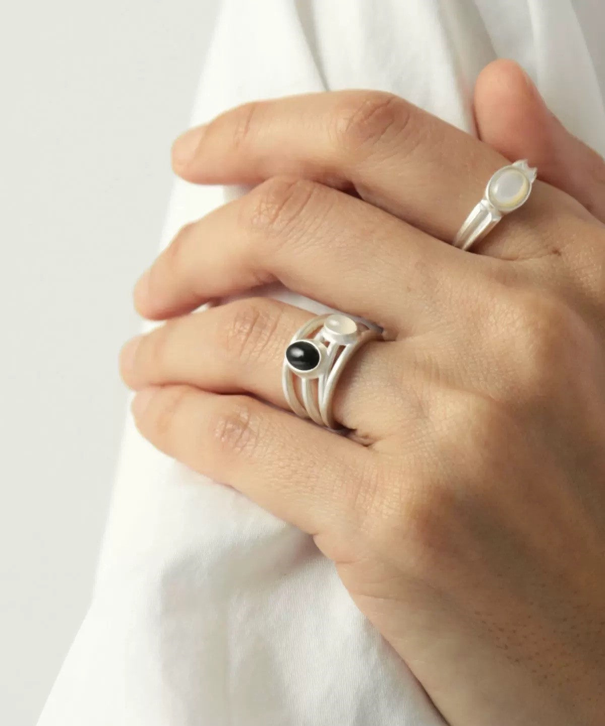 Close-up of a hand wearing two silver rings with gemstones on a white background