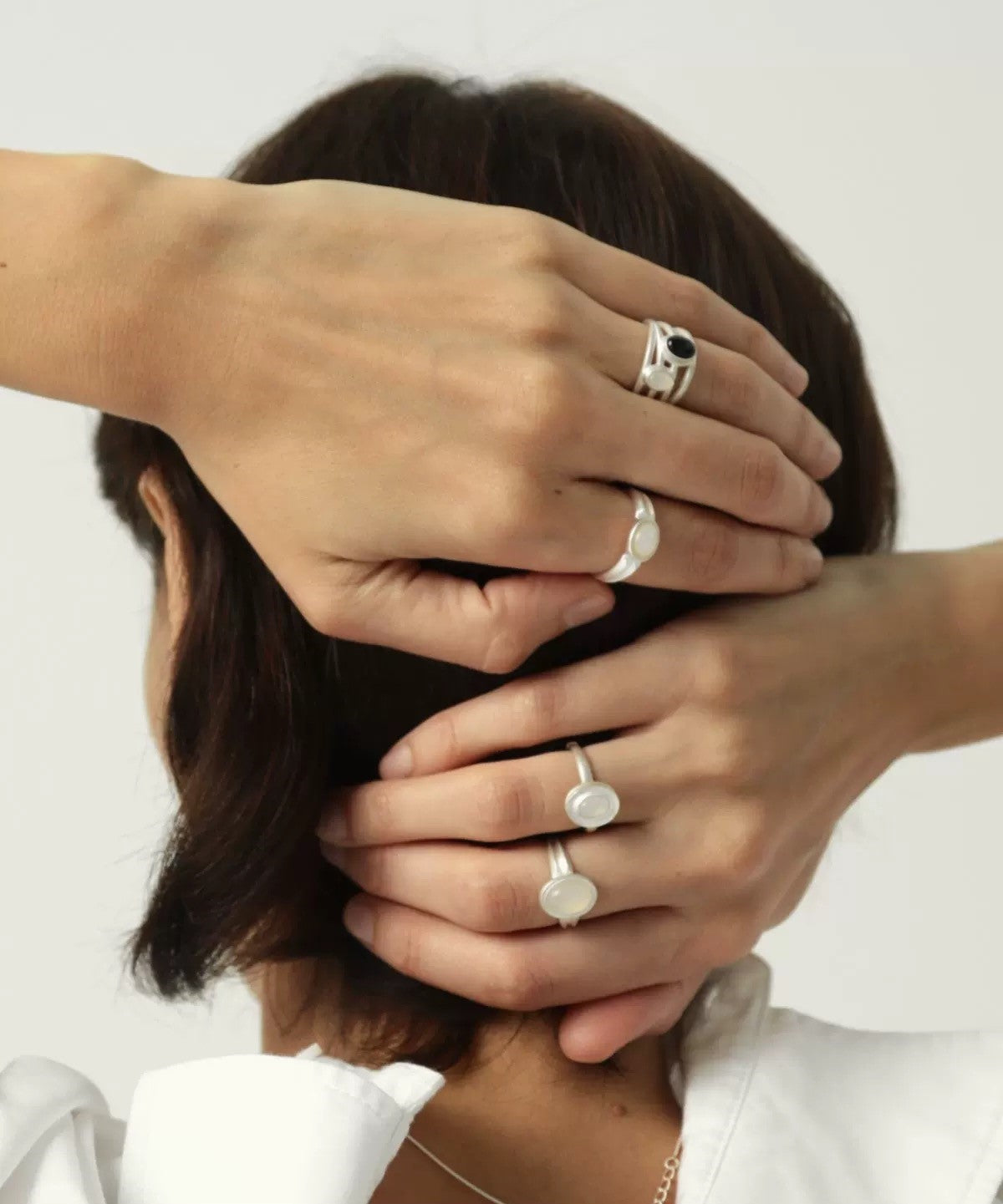 Close-up of a person wearing multiple silver rings on a plain background
