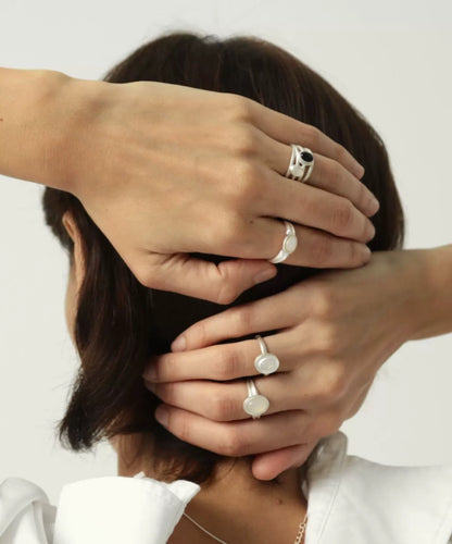Close-up of a person wearing multiple silver rings on a plain background
