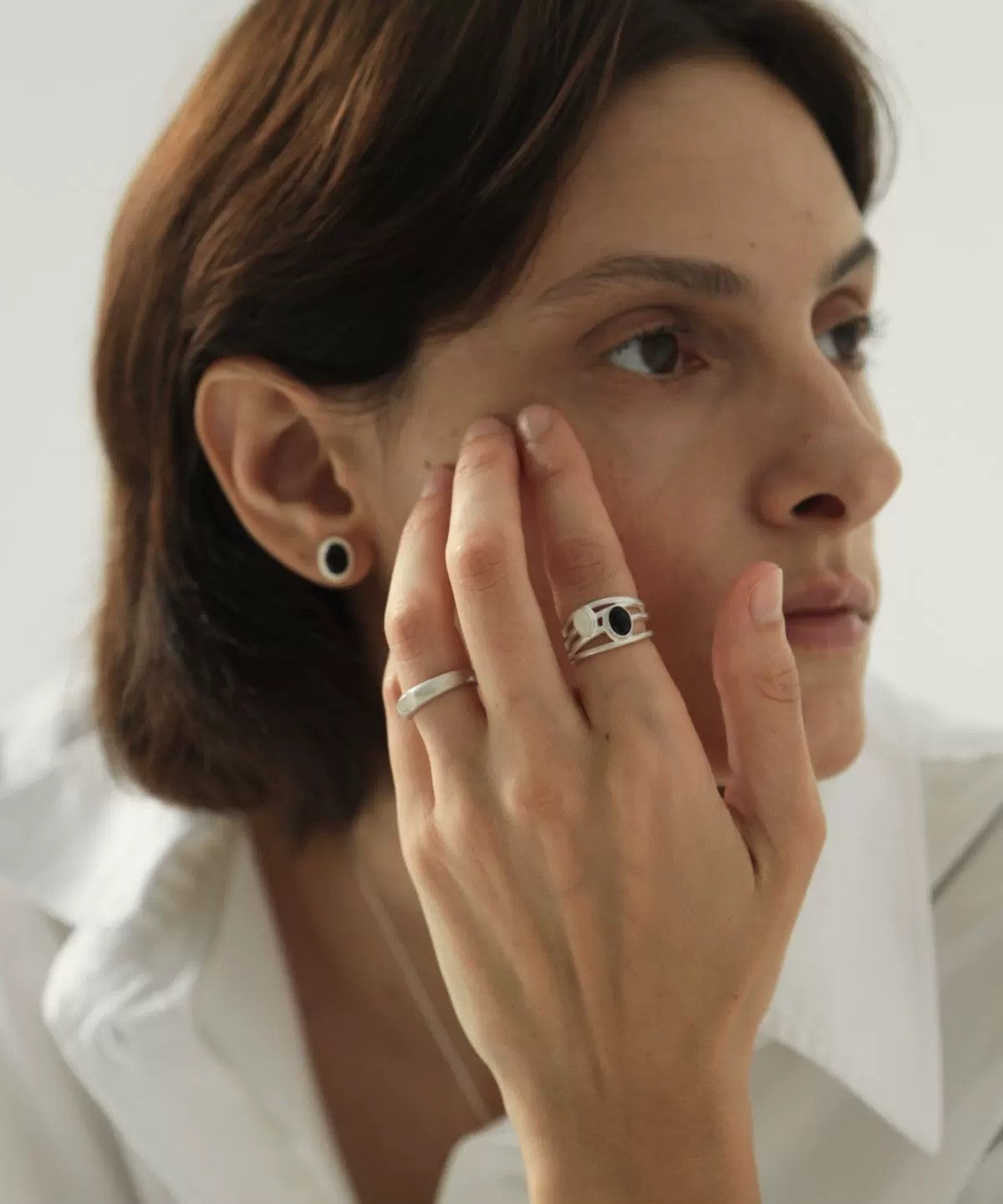 Woman wearing a silver ring with a black gemstone on her finger, with a plain background.