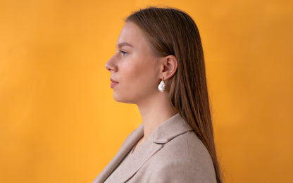 Woman wearing golden earrings with baroque pearls against an orange background