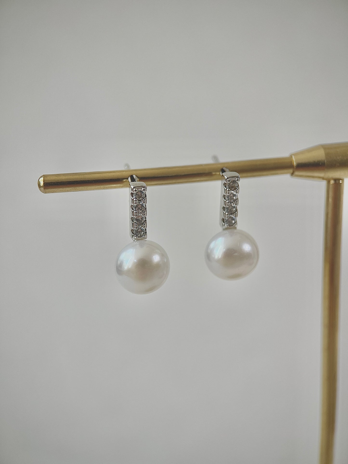 Pearl earrings with diamond accents on a gold stand against a light gray background