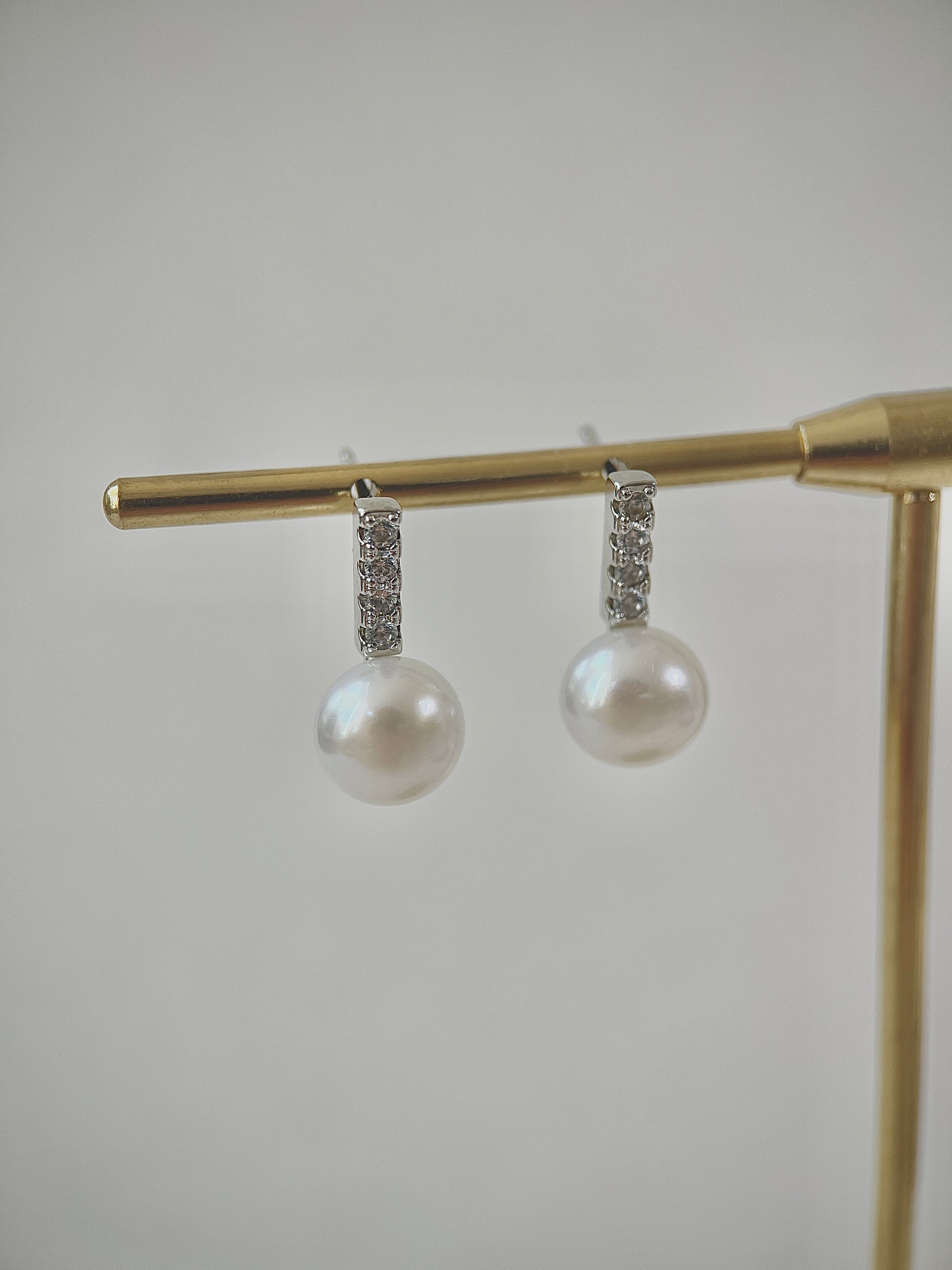 Pearl earrings with diamond accents on a gold stand against a light gray background