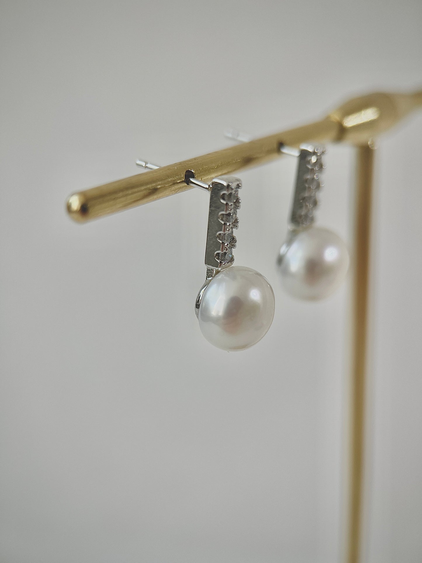 Pearl earrings hanging on a gold stand against a neutral background