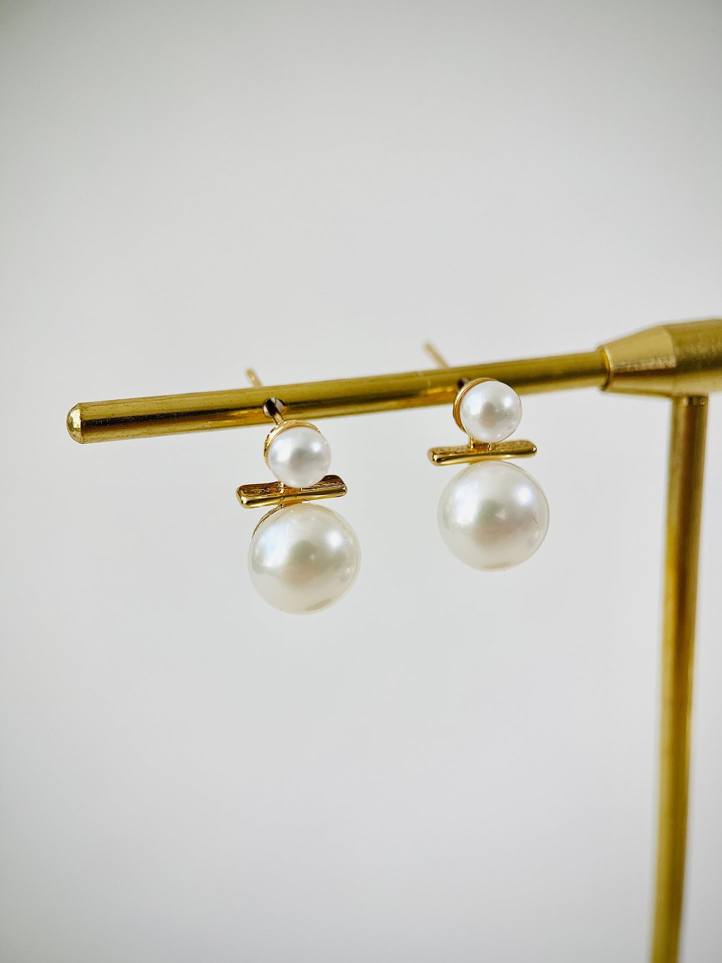 Pearl earrings on a gold stand against a light background