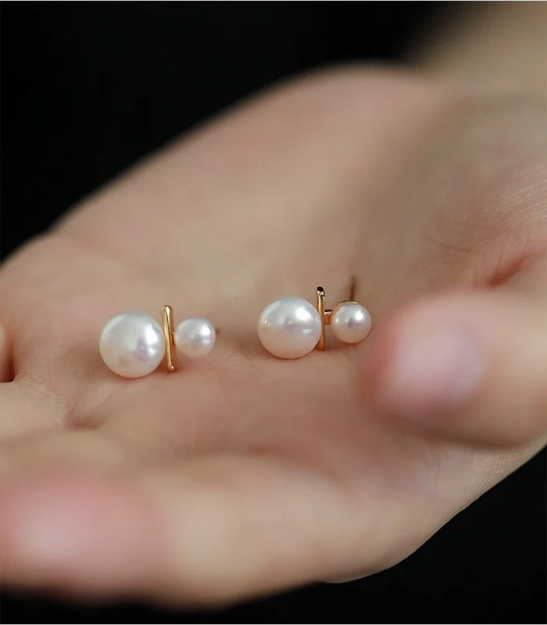 Pearl earrings displayed on a hand against a dark background