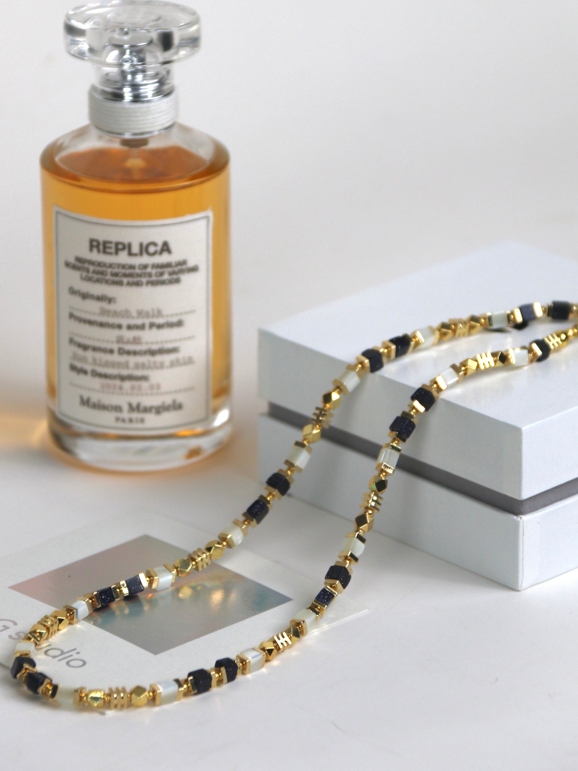 Perfume bottle labeled 'Replica' next to a necklace on a white surface