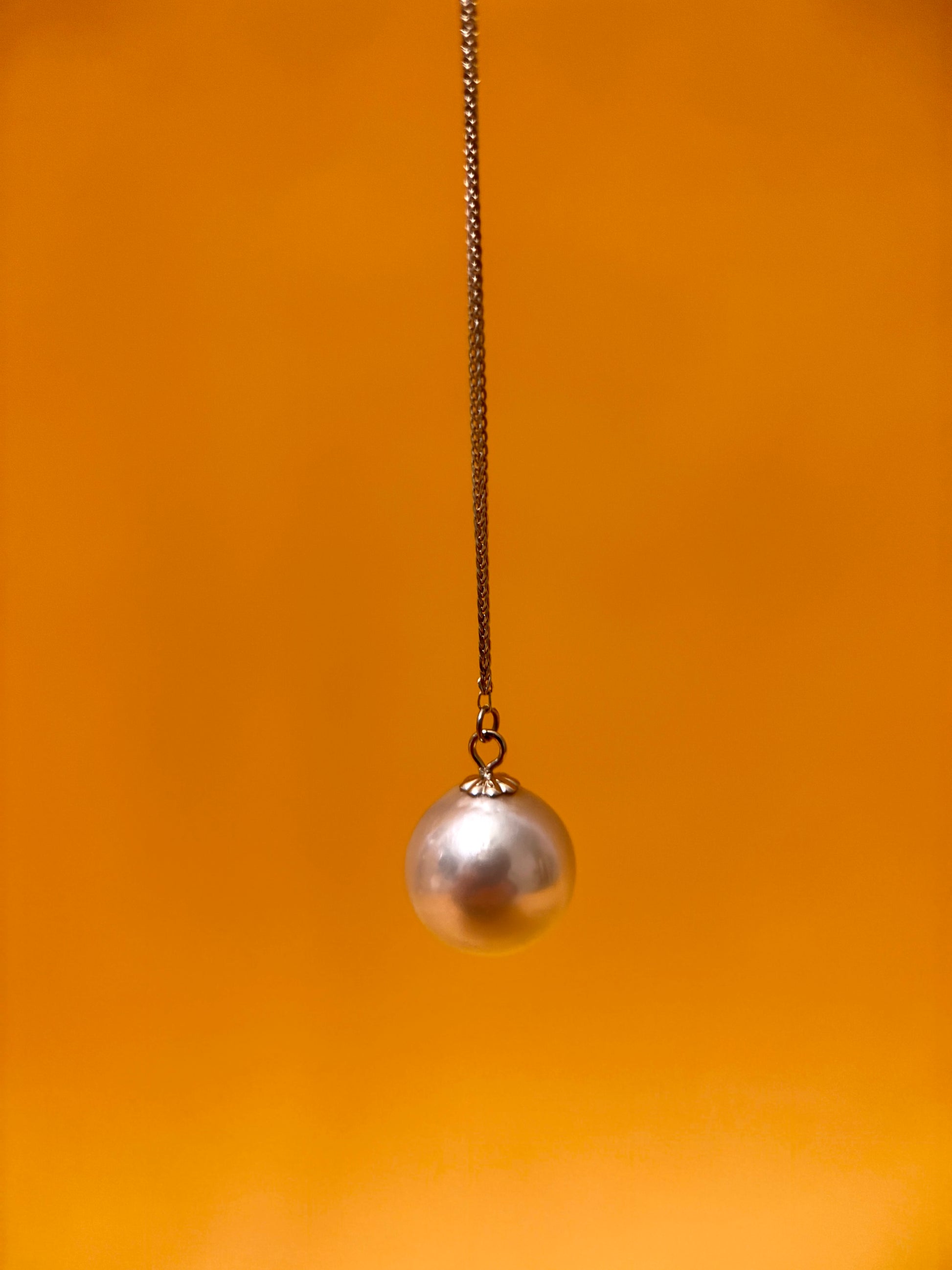 Akoya pearl pendant necklace hanging from a chain against an orange background.