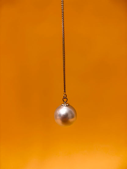 Akoya pearl pendant necklace hanging from a chain against an orange background.