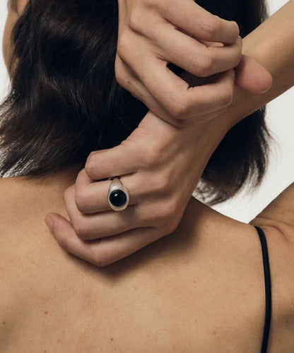 Close-up of a hand with a ring on a person's shoulder against a neutral background