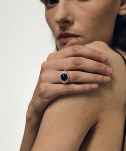 Close-up of a person's hand wearing a black ring on a plain background