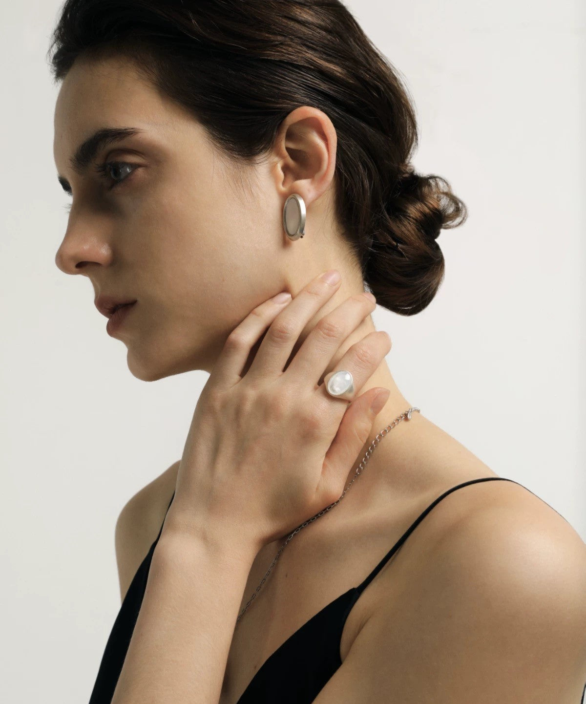 Woman wearing earrings and a ring on a plain background