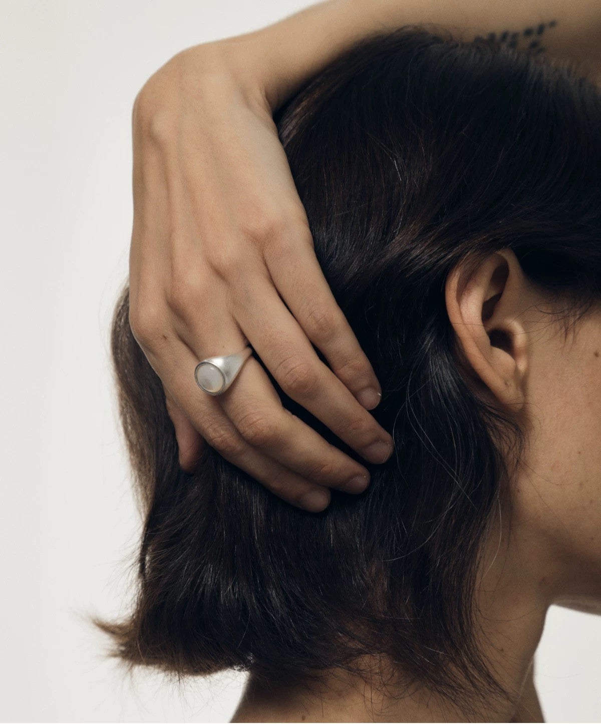 Person with hand on head wearing a silver ring against a neutral background
