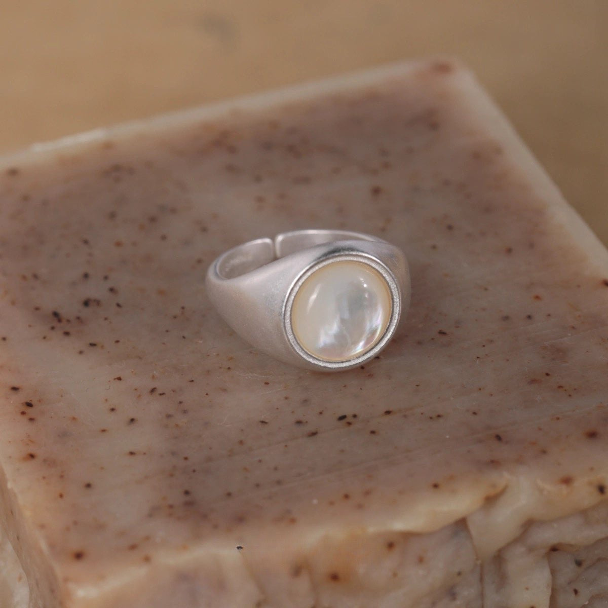 Silver ring with a central stone on a textured beige surface