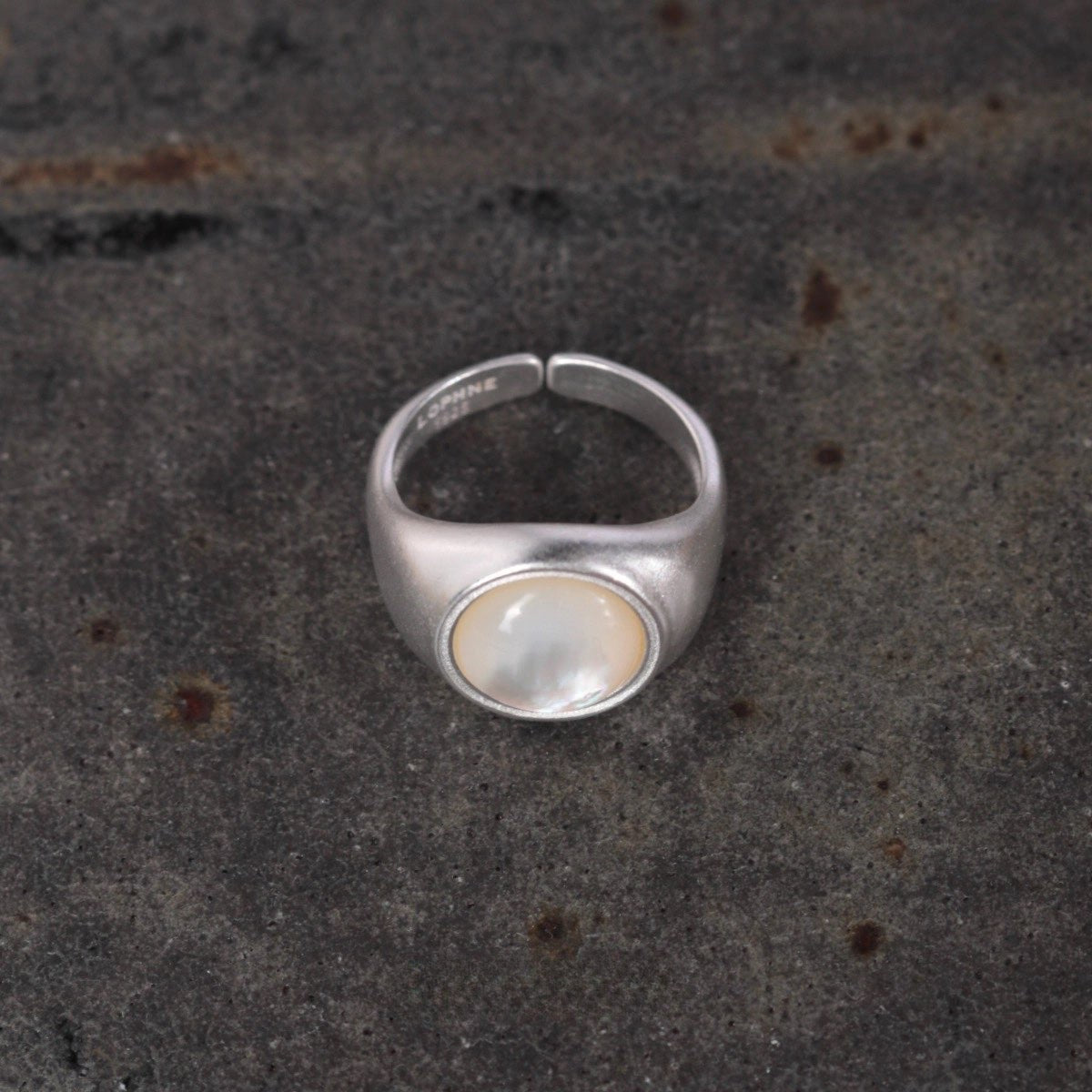 Silver ring with a central gemstone on a textured dark surface