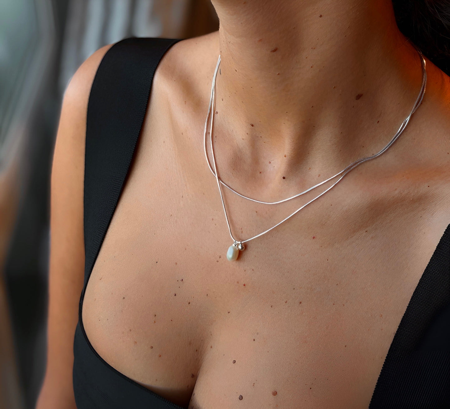 Close-up of a person wearing a silver necklace with a white pearl pendant.