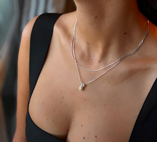 Close-up of a person wearing a silver necklace with a white pearl pendant.
