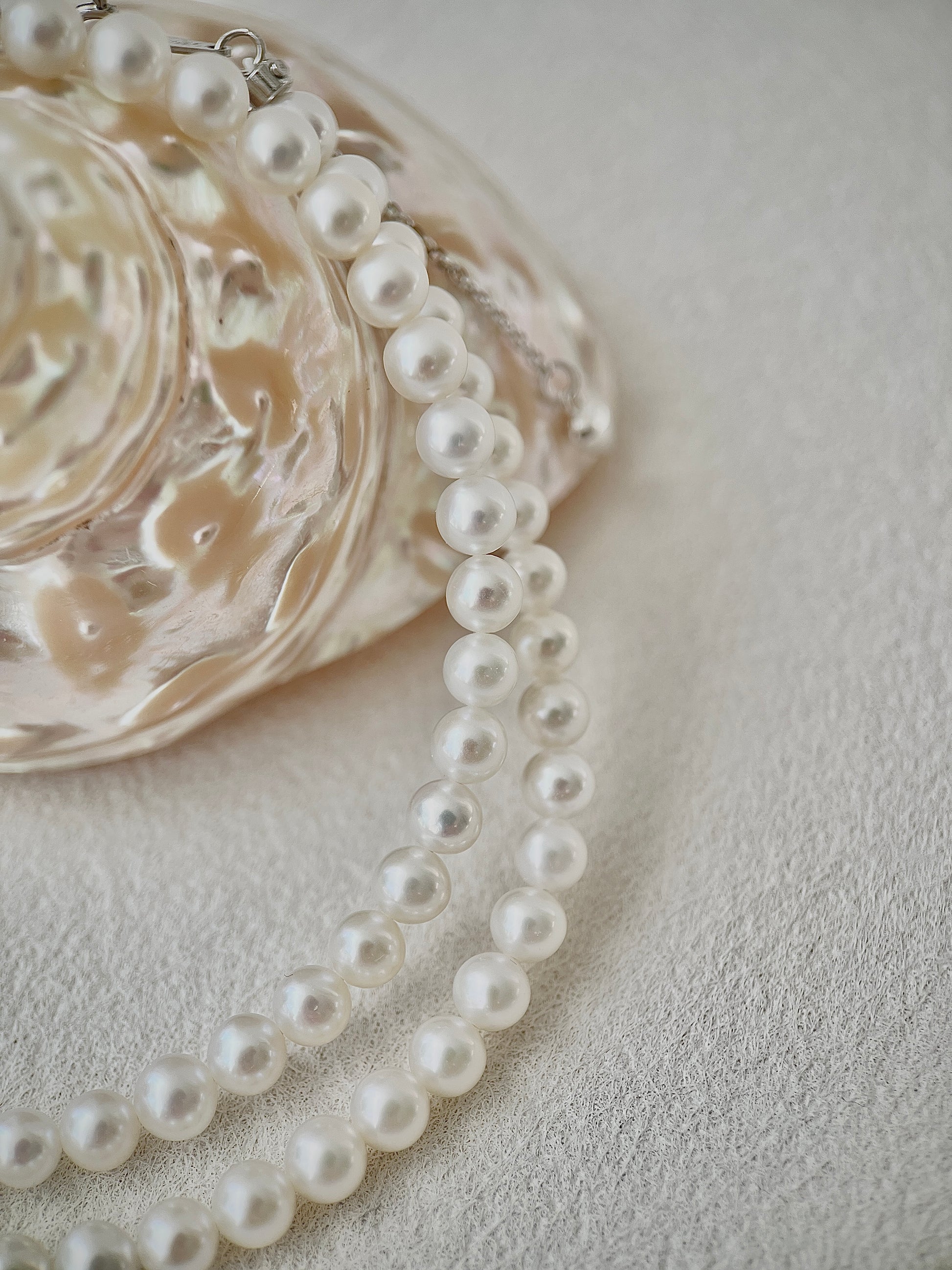 Pearl necklace on a textured surface with a decorative dish in the background