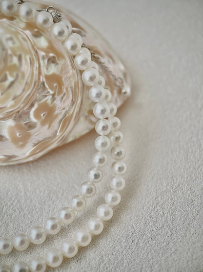 Pearl necklace on a textured surface with a decorative dish in the background