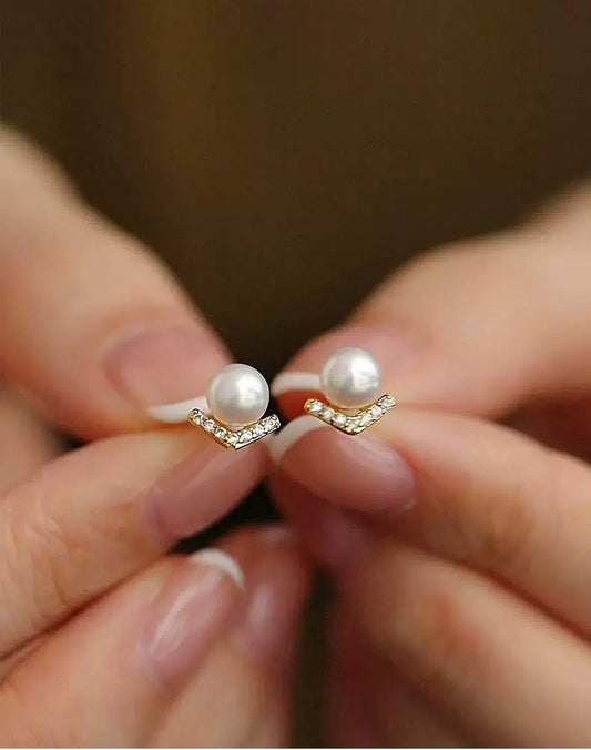 Pearl earrings held between fingers against a blurred background