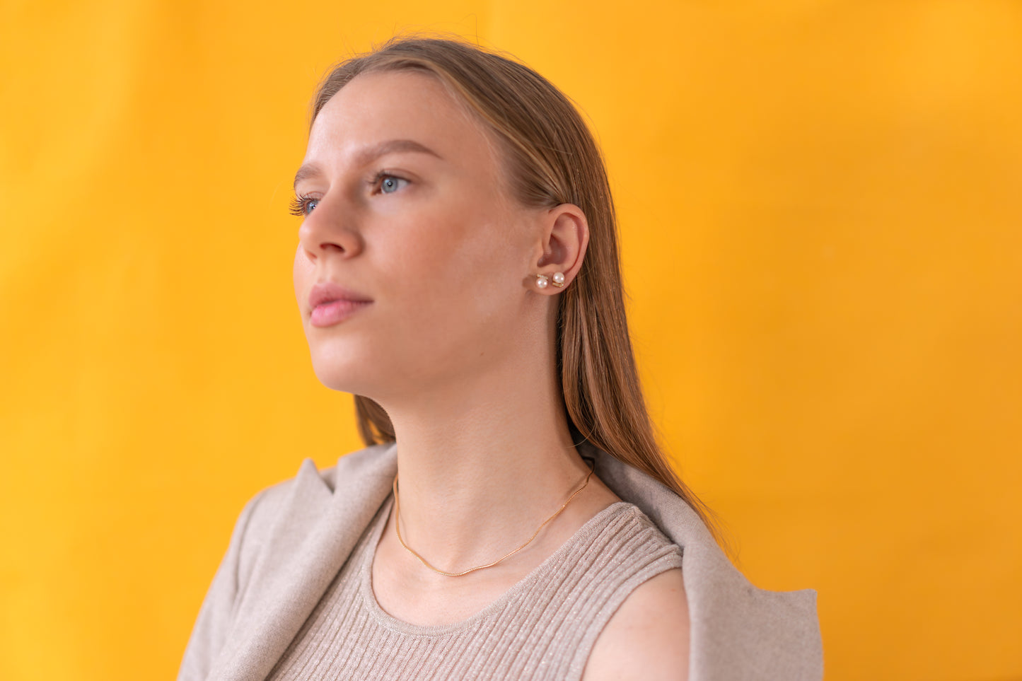 Woman wearing pearl earrings against a yellow background