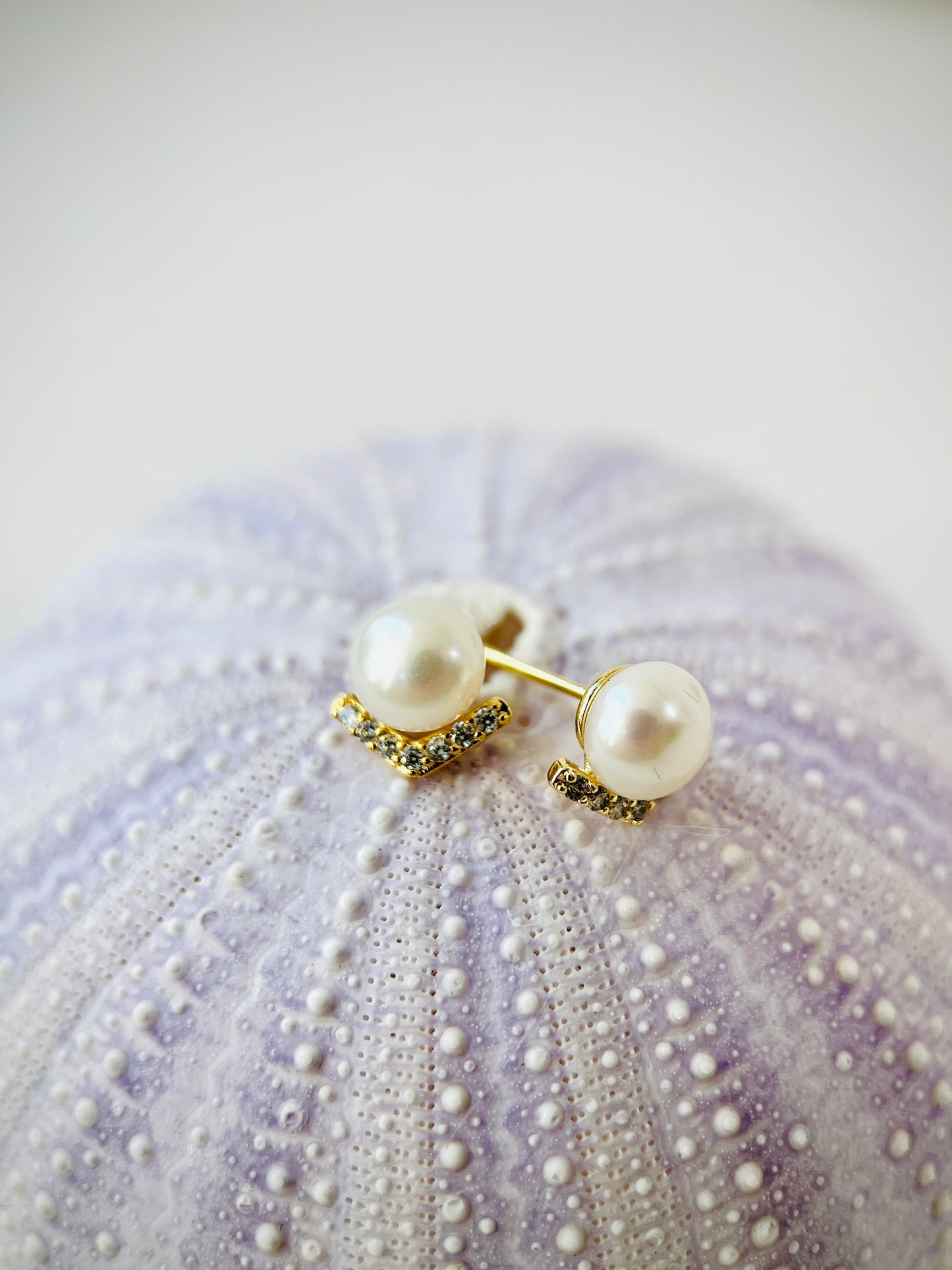 Pearl earrings with gold accents on a textured purple surface