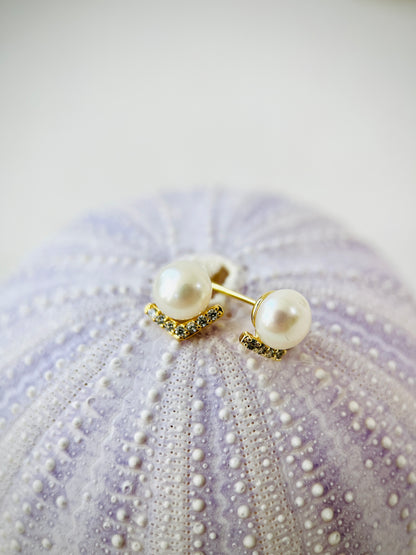 Pearl earrings with gold accents on a textured purple surface