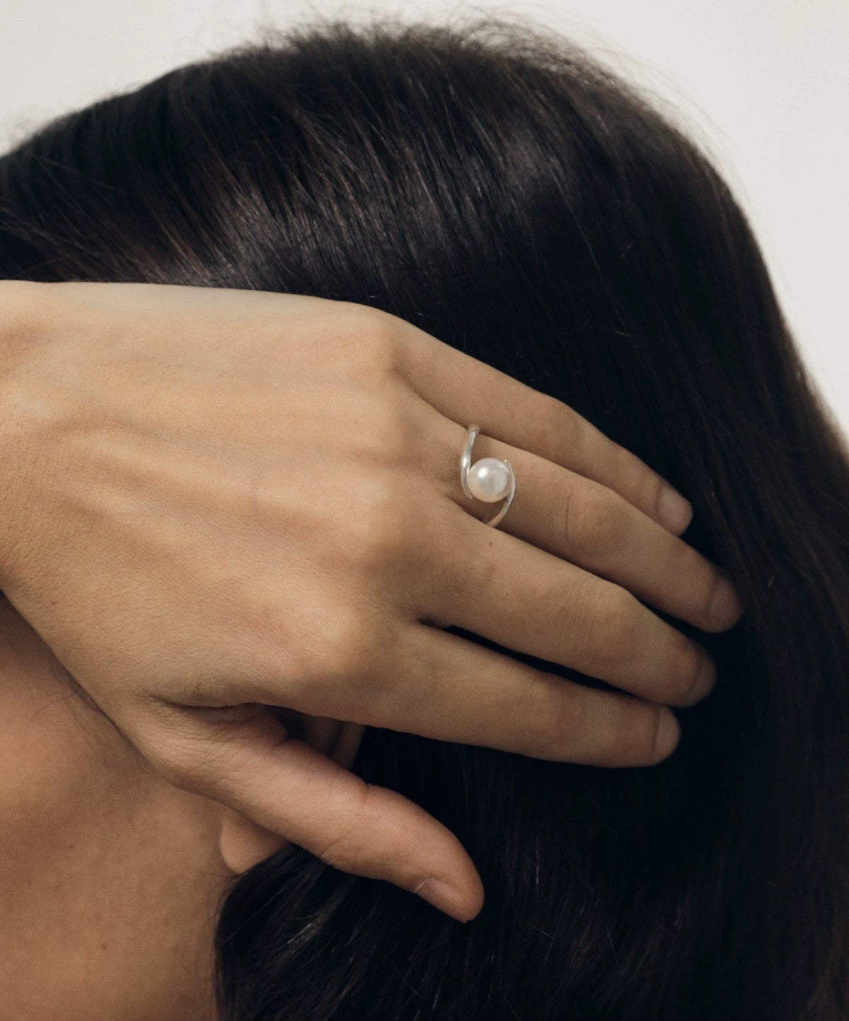 Hand with a pearl ring holding dark hair against a neutral background