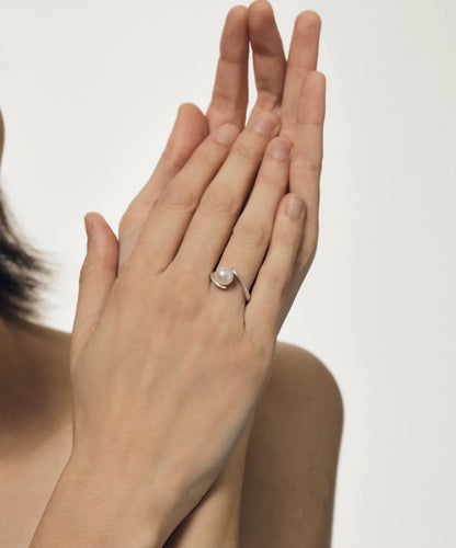 Hand wearing a pearl ring on a plain background