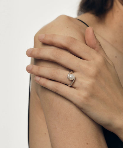 Close-up of a hand wearing a pearl ring on a neutral background