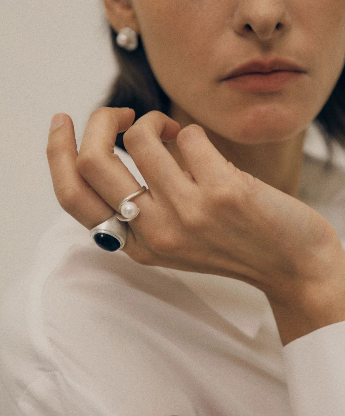 Close-up of a person wearing two rings with pearls on a plain background