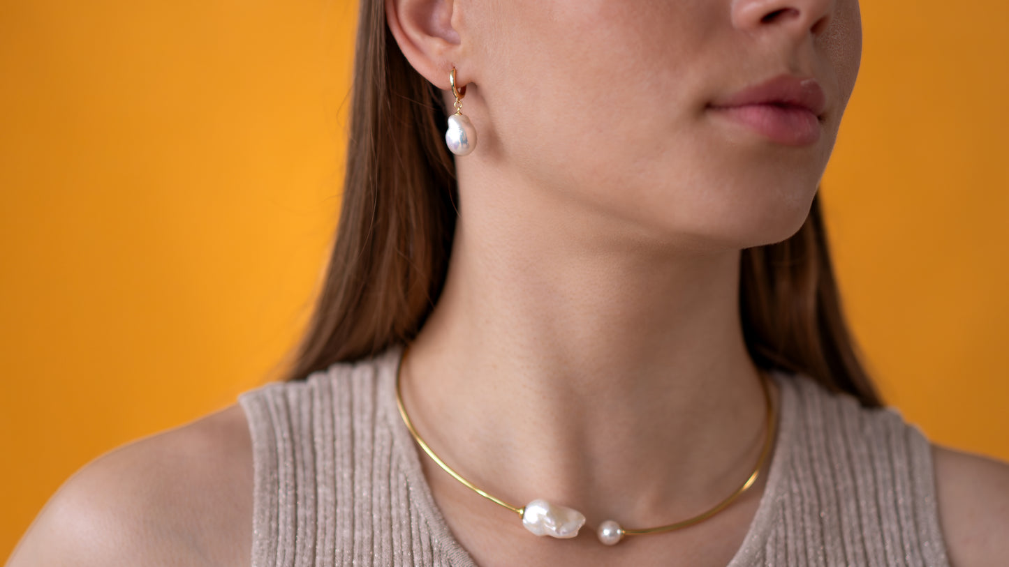 Woman wearing a gold necklace and pearl earrings against an orange background