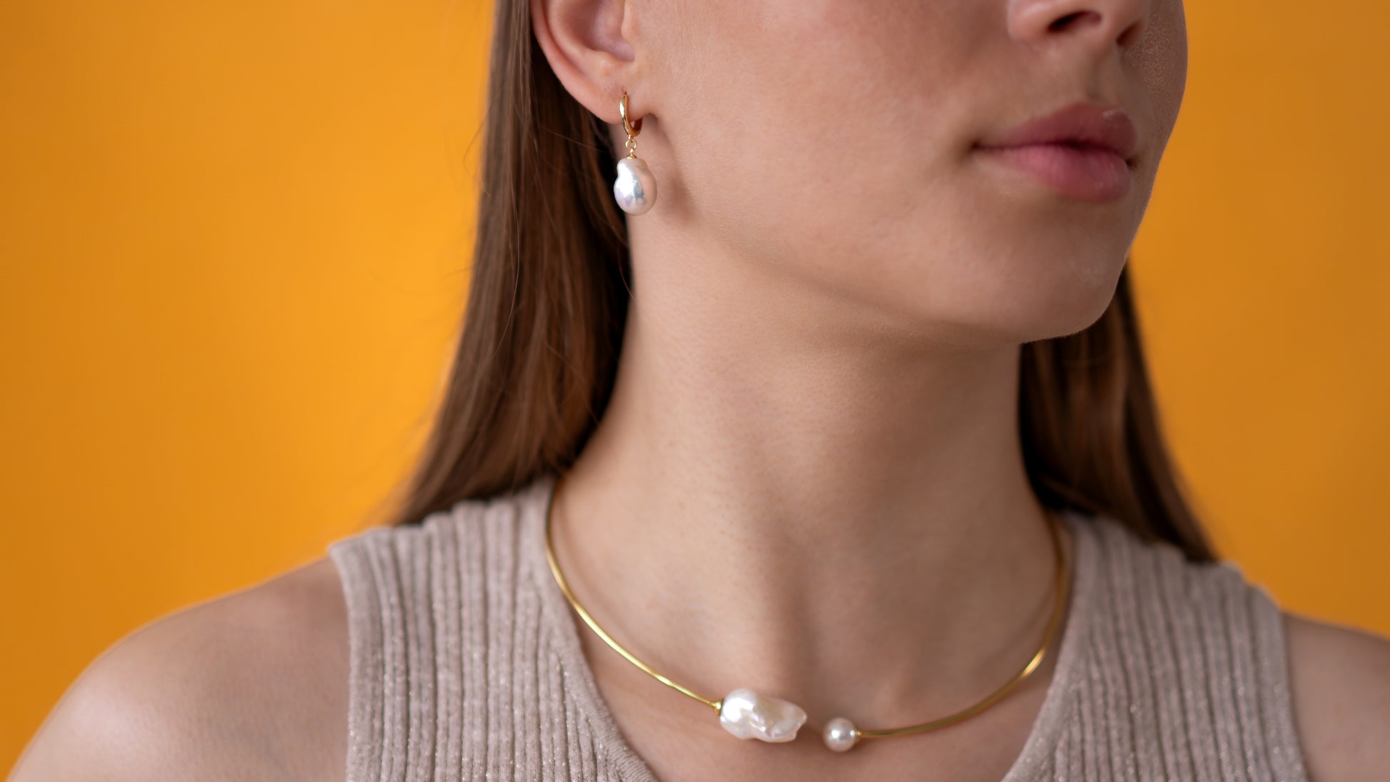 Woman wearing a gold necklace and pearl earrings against an orange background