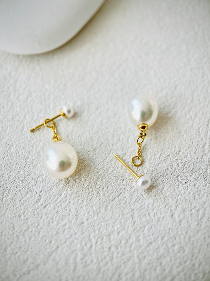 Pearl earrings with gold hooks on a textured white surface