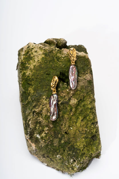 Gold and pearl earrings on a textured green surface