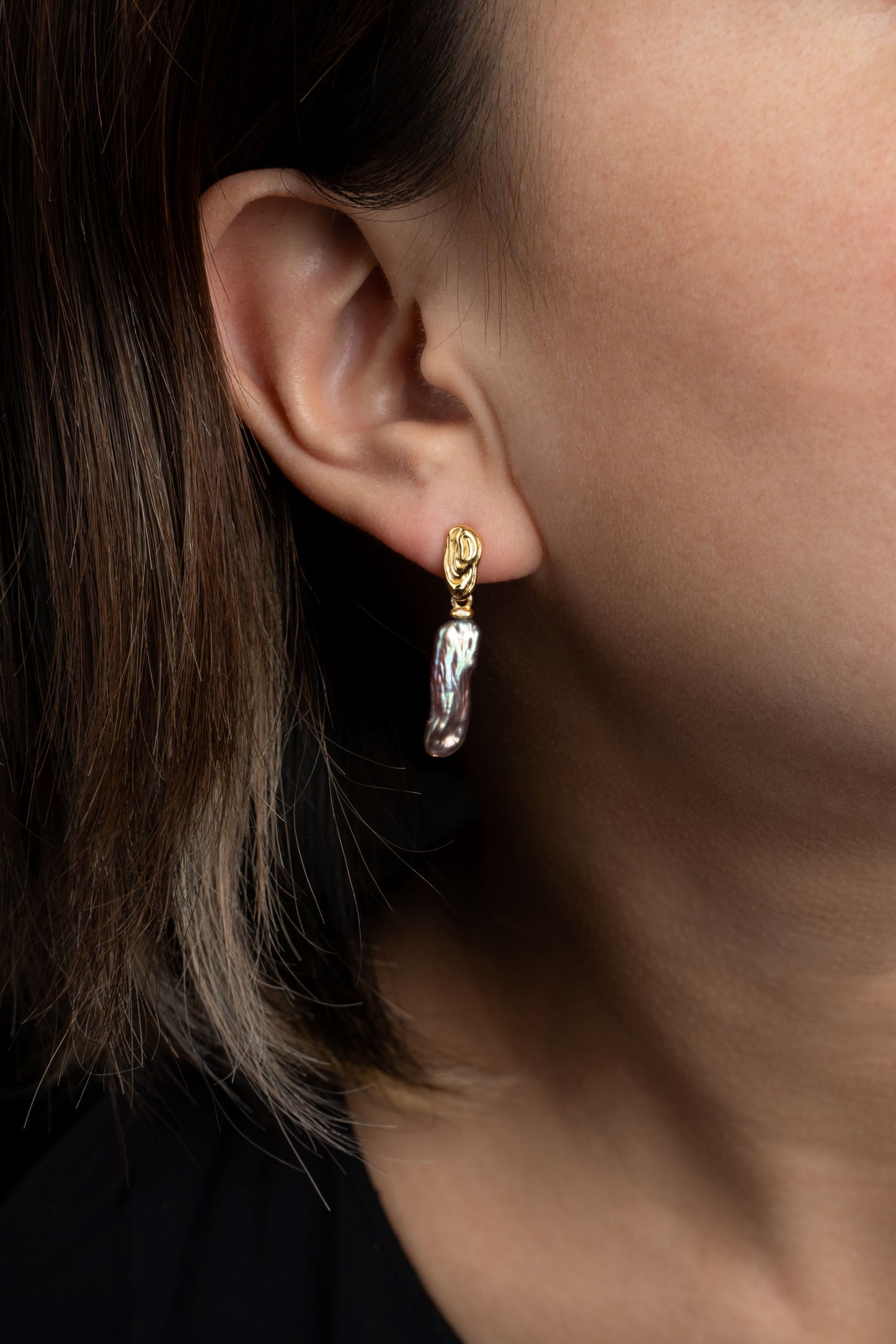 Close-up of a person wearing a pearl earring with a dark background