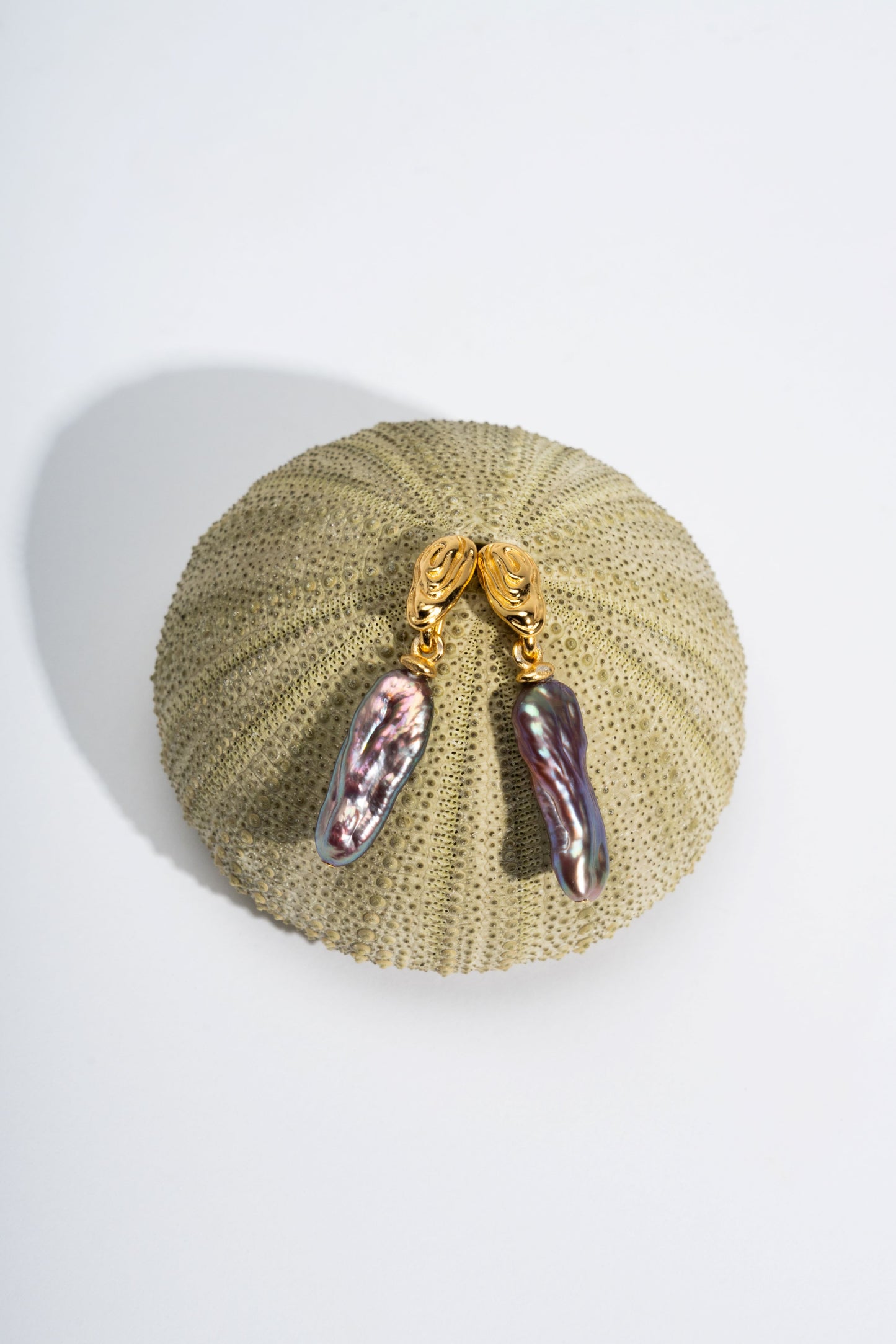 Pair of earrings with pink and purple pearls on a textured beige surface