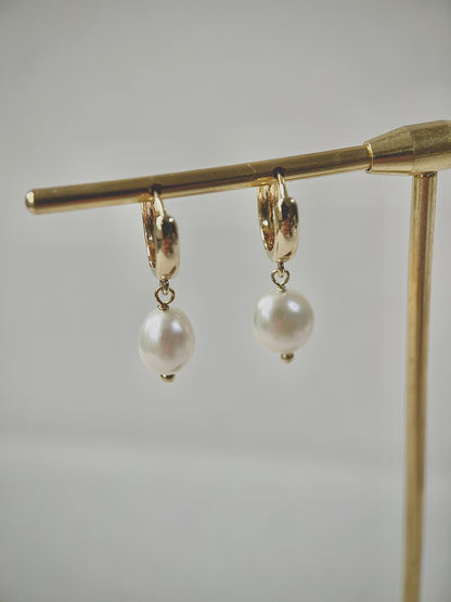 Gold hoop earrings with pearl drops on a gold stand against a light gray background